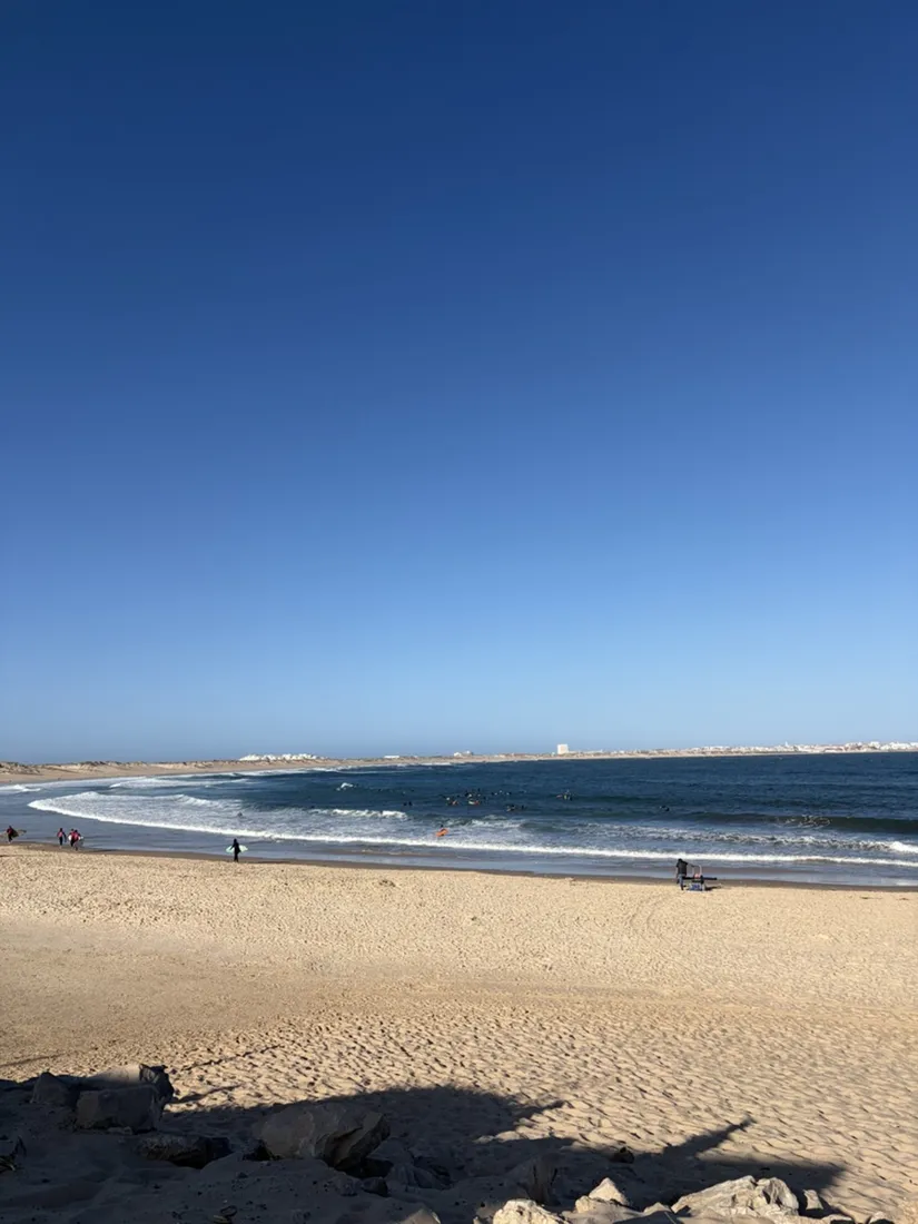 Surfer in der Brandung unterhalb der Dünen, gegenüber die Halbinsel von Peniche