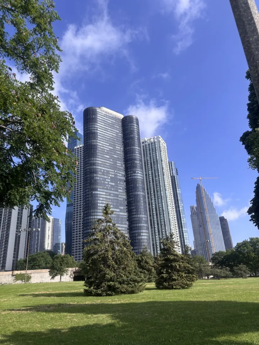 Curved downtown towers rising over a Grant Park lawn, seen from the lakefront trail